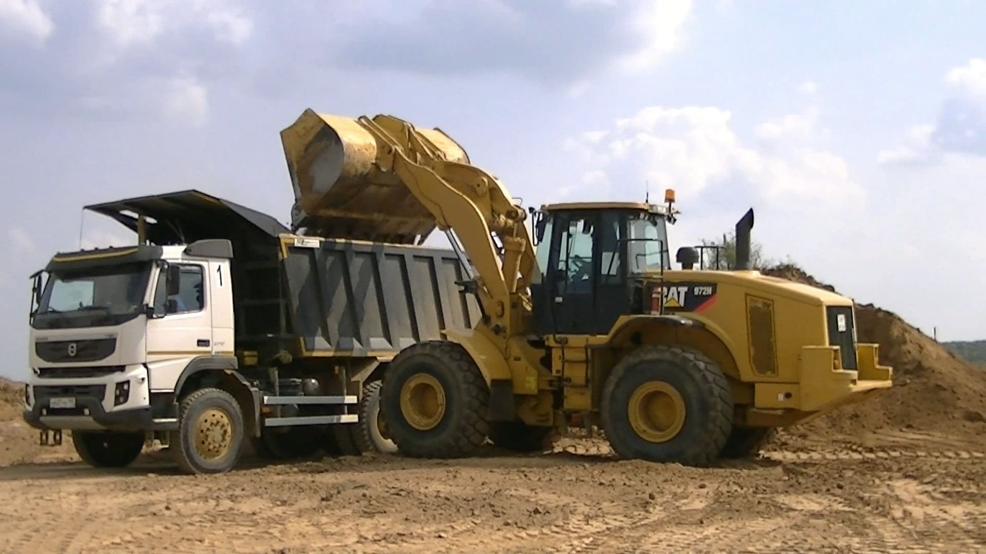 Погрузчик Cat 972H грузит самосвалы Volvo FMX