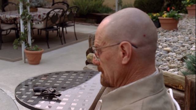 Отрывок из сериала во все тяжкие мужчина Уолтер Уайт сидит за столом крутит пистолет