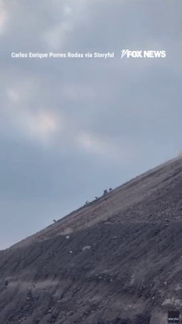 Туристы мчатся вниз по склону гватемальского вулкана в то время как он извергает пепел