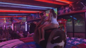 Две девушки в юбках пытаются оседлать механического быка (КДН)