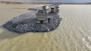 Строительство дороги на озере. Самосвалы сгружают камни
