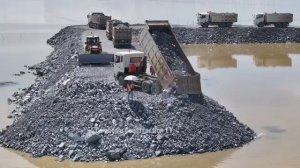 Строительство насыпной дороги. Подвоз камней и грунта самосвалами, разравнивание их бульдозером