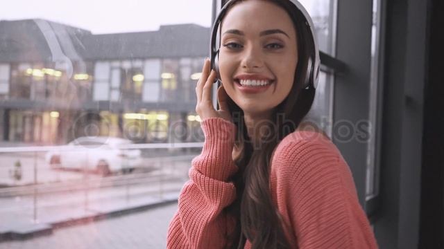 Beautiful young woman standing near window and dancing while listening music in headphones смотреть онлайн