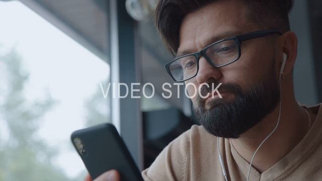 Modern man is talking on video, using smartphone and headphones. смотреть онлайн