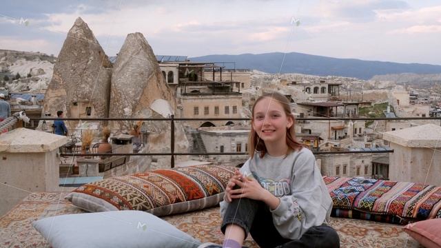 Cheerful young girl sitting on terrace and smiling at camera in Cappadocia смотреть онлайн