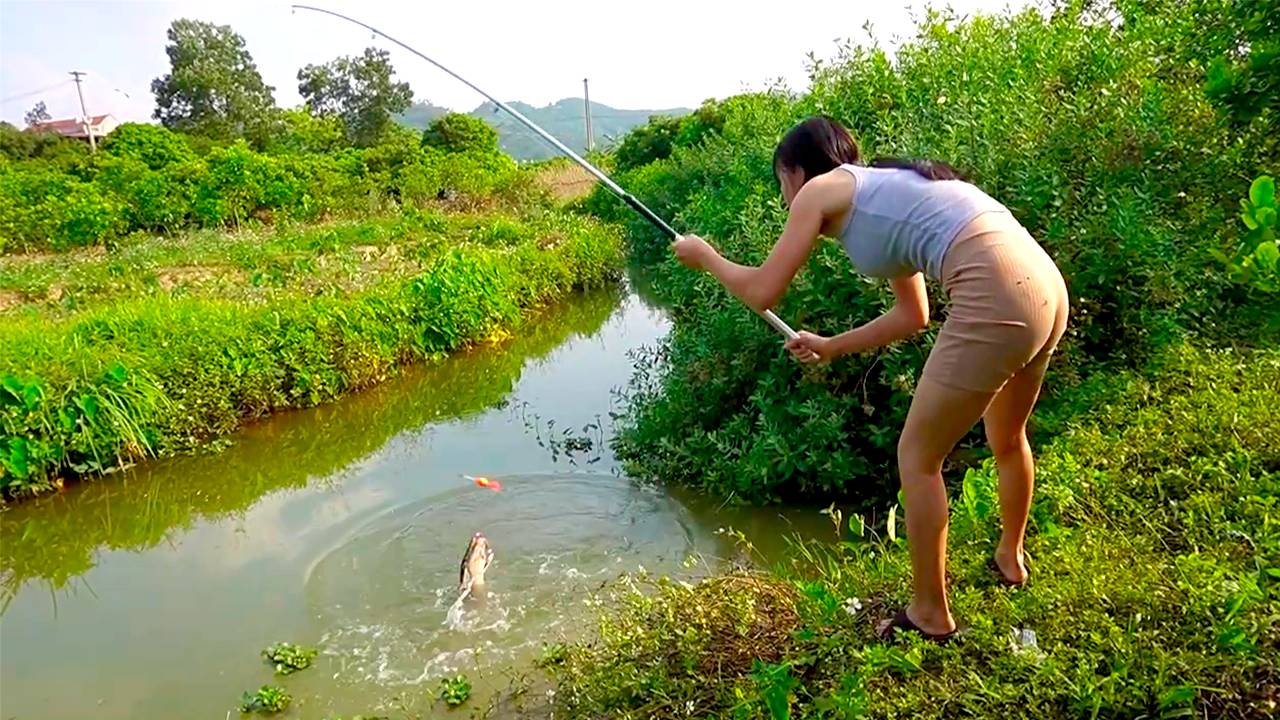 Рыбалка Красивая Девушка ловит крупную рыбу сома в маленьком пруду на удочку с поплавком