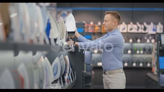 A Young Handsome Man in a Shirt Chooses an Iron in a Consumer Electronics Store. Bachelor | Stock смотреть онлайн