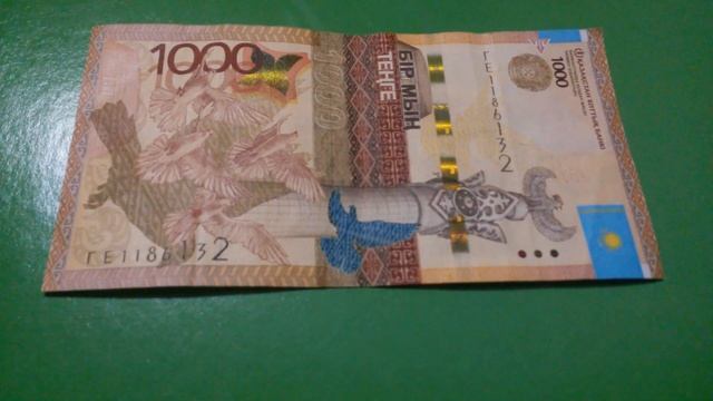 БАНКНОТА 1000 ТЕНГЕ № серии ГЕ1186132 на зелёной поверхности Седьмого Января - ДЕНЕЖНЫЙ ПОТОК