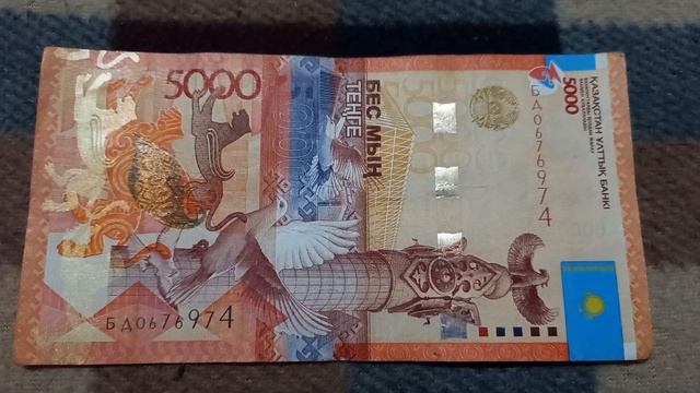 БАНКНОТА 5000 ТЕНГЕ № серии БД0676974 на байковой поверхности 22-ого Октября - ДЕНЕЖНЫЙ ПОТОК