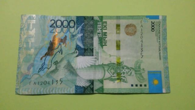 БАНКНОТА 2000 ТЕНГЕ № серии ГА1204135 на салатовой поверхности 30-ого Января - ДЕНЕЖНЫЙ ПОТОК