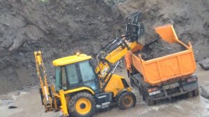 Экскаватор погрузчик загружает Камаз под дождём и пое