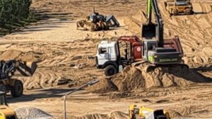 Погрузчик перевозит песок в ковше и выгружает