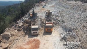 Строительство новой дороги в горах: грузовик сыплет крупные камни, экскаватор загружает.