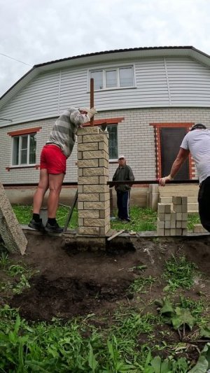 Бригада каменщиков строит забор из рваных кирпичей.
