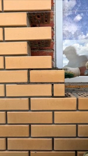 Каменщик пилит кирпич ножовкой и делает оконные проемы нужного размера.