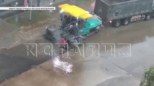 Стоя по колено в воде дорожные рабочие кладут асфальт на дорогу