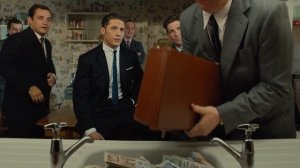 Момент из фильма Легенда Том Харди в костюме мужчины идут по кругу кладут деньги в раковину