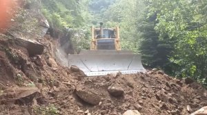 Бульдозер KOMATSU D85EX прокладывает дорогу в каменистом лесу.