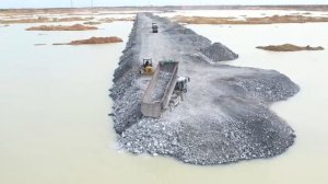 Отсыпка дороги на озере. Бульдозер толкает камни.