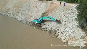 Экскаватор и самосвал работают над обрезкой (профилированием) грунтового склона в русле реки.