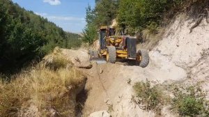 Грейдер CAT 140M засыпает канаву на дороге.