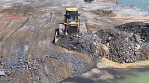 Расширение берега озера на 200 метров и строительство дороги — бульдозер толкает камни в воду.