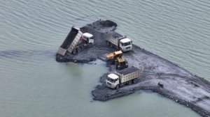 Самосвал SHACMAN перевозит щебень для строительства дороги на озере с помощью колесного погрузчика.