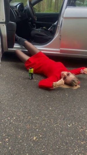 Блондинка лежит на асфальте с энергетиком в колготках на каблуках