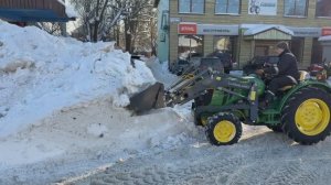 Минитрактор John Deere c погрузчиком чистит снег