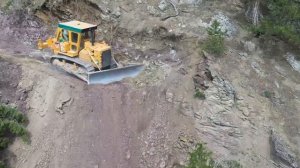 CAT D7 BULLDOZER пробивает дорогу в опасном месте в горах.