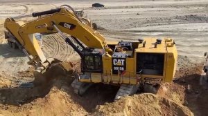 Экскаватор Cat 6015B мощно черпает вскрышу, наполняя самосвал, рядом элегантно скользит грейдер Cat