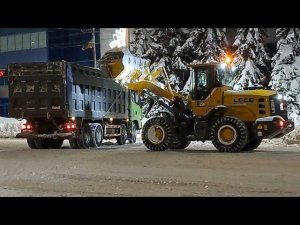 Трактор погрузчик загружает снег в самосвал