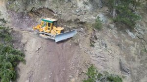 Экскаватор и бульдозер пробивают дорогу через горы.