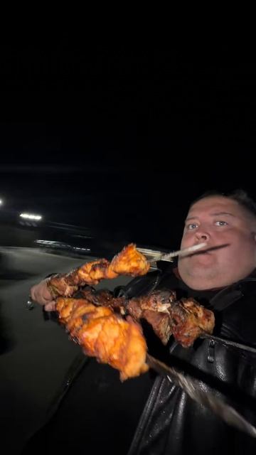 Мужчина сидит на карусели крутится держит в руке шампуры с мясом шашлык