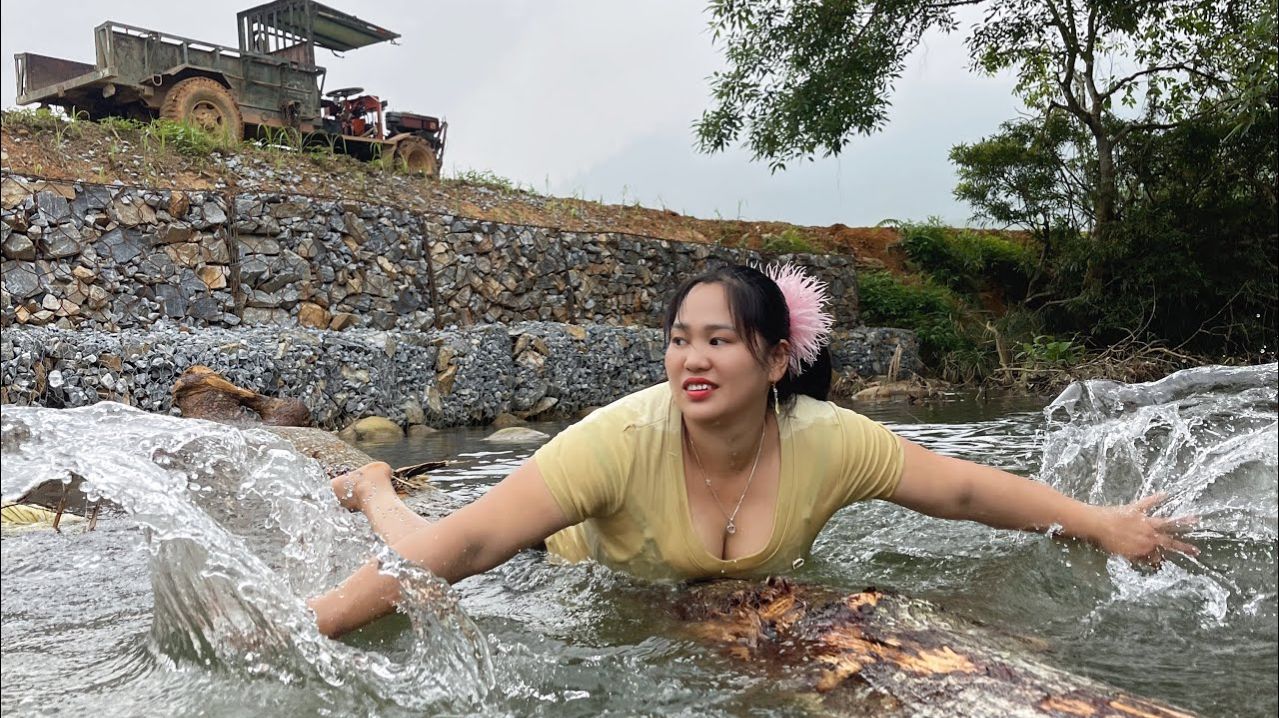 Сельскохозяйственная техника перевозит древесину, девушка купается в прохладной зеленой реке.