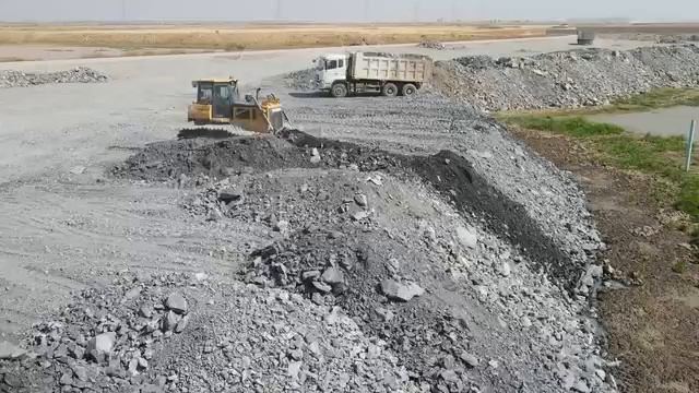 Бульдозер и самосвалы засыпают огромную территорию.