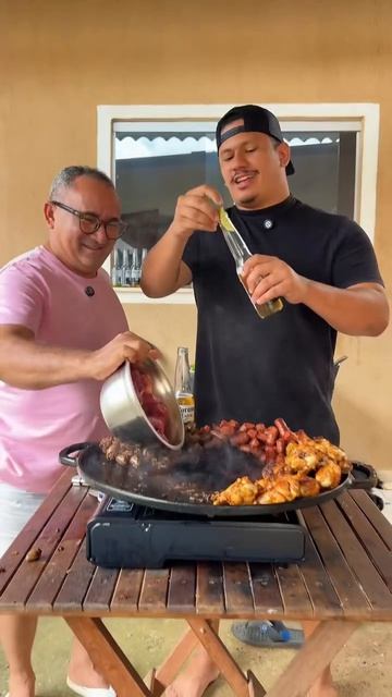 Двое мужчин на улице у столика, во дворе жарят мясо/шашлык и пьют напитки, танцуют