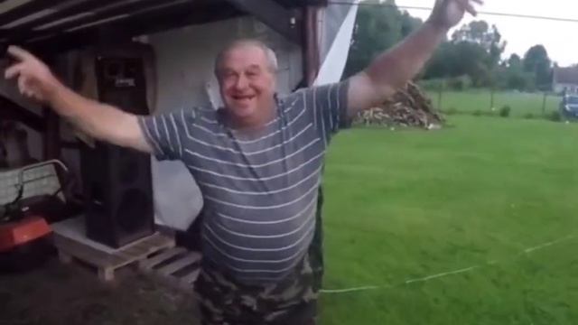 Мужчина в серой голубой футболке в полоску танцует руками в деревне Мем