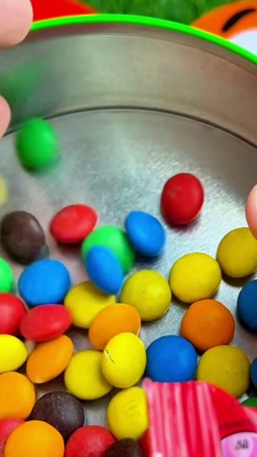 Удовлетворяющее высыпание конфет M&M's в зеленую банку