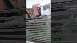 Ловкая работа водителя мусоровоза по очистке мусорных баков на территории овощного рынка.