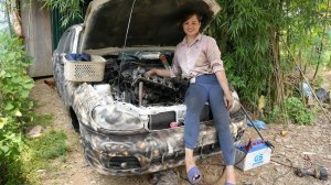 Девушка чинит, реставрирует и обслуживает сильно поврежденный автомобиль-металлолом