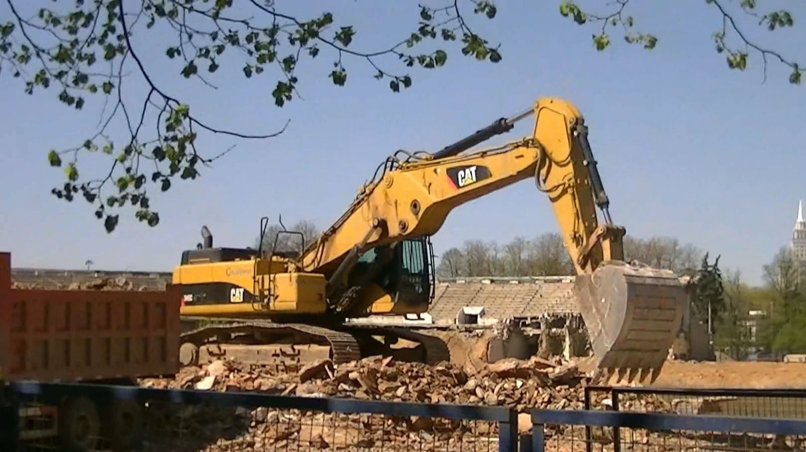 Экскаватор Cat 345C L грузит обломки трибун стадиона