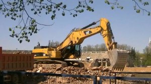 Экскаватор Cat 345C L грузит обломки трибун стадиона