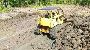 Бульдозер Caterpillar D6D равномерно разравнивает глину в лесу.