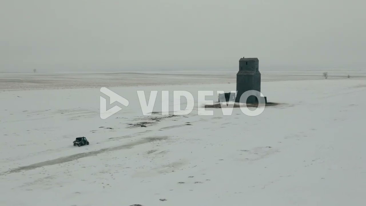 Аэрофотосъемка UTV бок о бок приближающегося к зданию в заснеженных прериях зимой, 4K