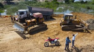 Самосвал закопался в песок при строительстве насыпной дороги. Бульдозер пытается его вытащить