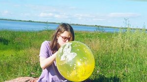 Симпатичная девушка тренирует лёгкие (надувает жёлтый шарик) на природе