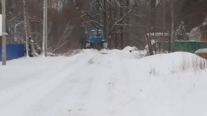 Трактор Т-150 чистит дорогу по улице в деревне