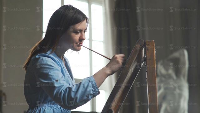 A young woman paints a painting on a canvas, standing behind an easel смотреть онлайн