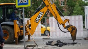 Экскаватор с отбойным молотком разбирает асфальт а рабочие стоят и смотрят